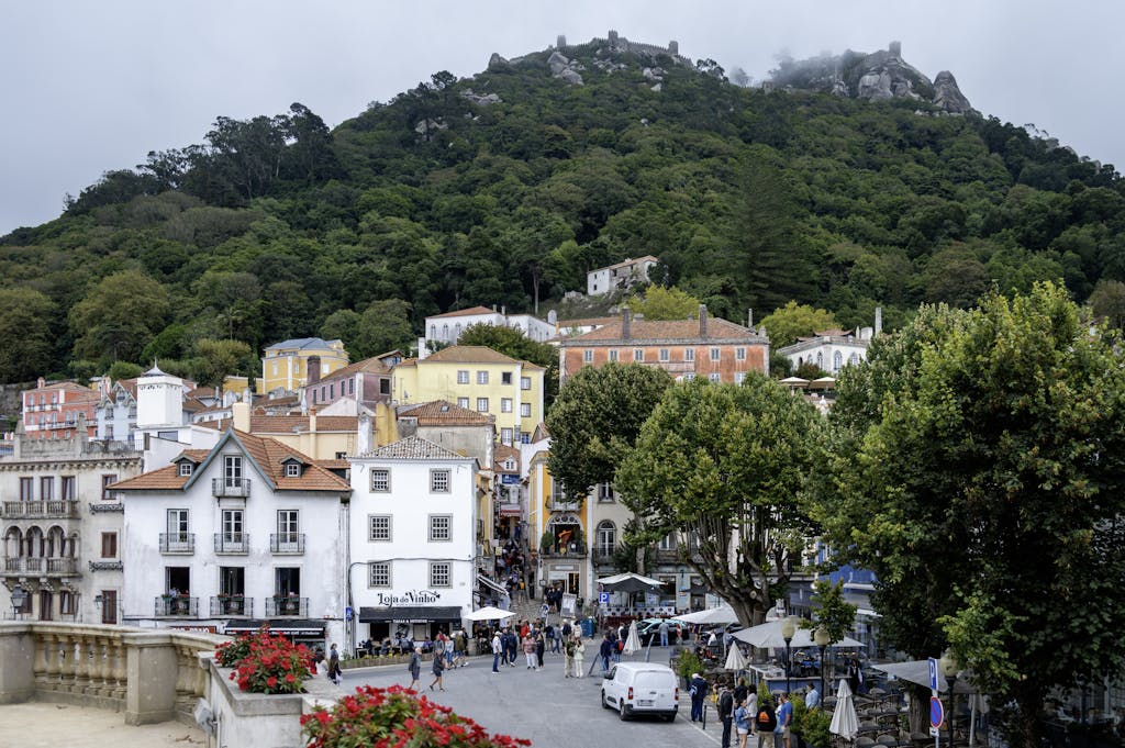 Vibrant street scene in Sintra, Portugal, showcasing colorful buildings and the Moorish Castle on a lush hillside.